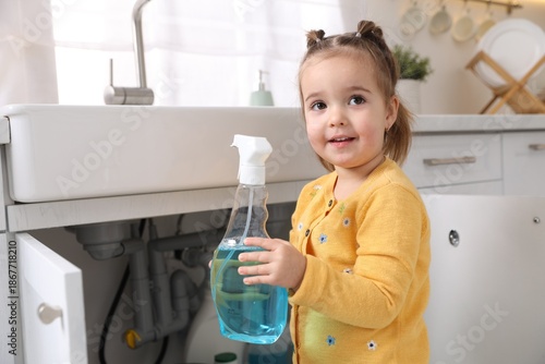 Child safety at home. Little girl with bottle of cleaning product in kitchen