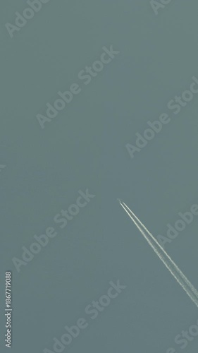 Twin contrails streak across clear blue sky with distant jet