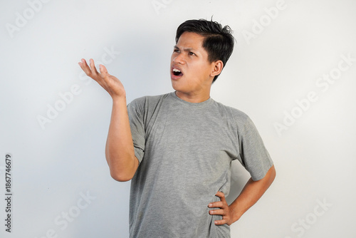 Photography A man wearing a gray shirt stands against a neutral backdrop, gesturing with an open hand and a frustrated, confused expression