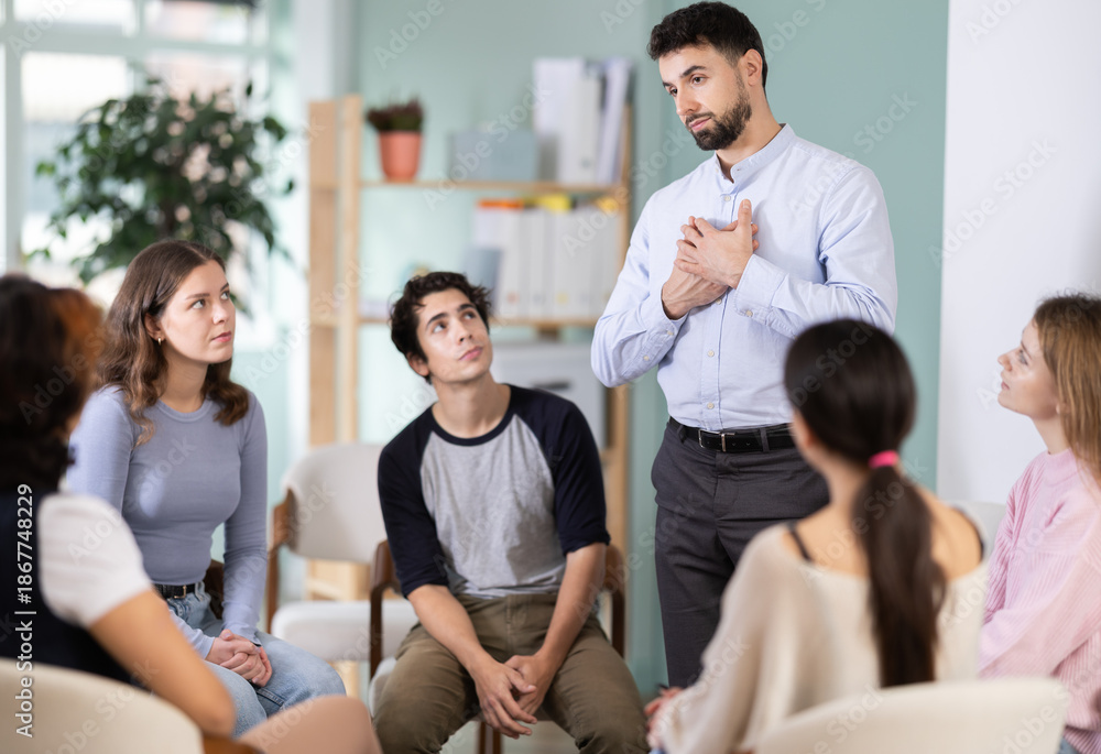 Fototapeta premium Active male teacher standing and talking to interested students sitting in a circle indoors