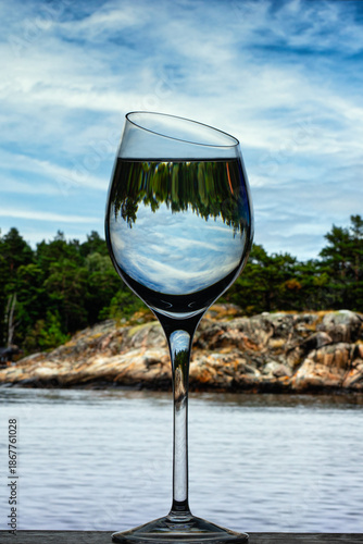 A glass goblet with clear water against the backdrop of the island's rocky shore
