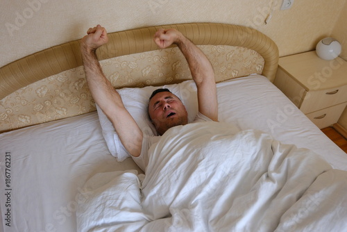 man stretching on bed in cozy bedroom with soft lighting and minimalistic decor featuring books and a small lamp. High quality photo