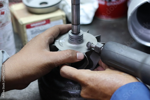 Obraz na plátne Close-up of a technician's hands using a professional rotary burr die grinder to clean and finish a metal turbocharger turbine wheel in a mechanical workshop