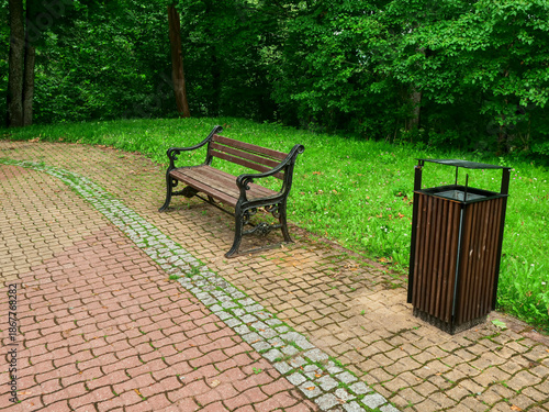 Foto A park bench sits on a brick path next to a trash can