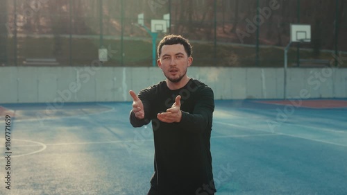Athletic man in a black long-sleeve shirt reaching toward the camera with open hands on a blue court. Warm sunlight backlight creates a cinematic rim light.