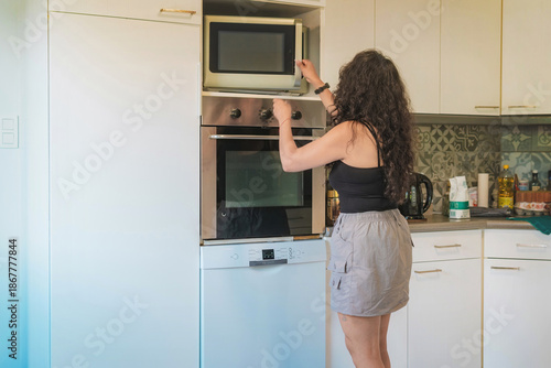 Middle-aged woman in her kitchen baking, she is opening the oven