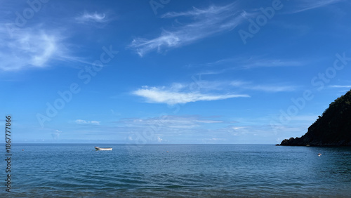 Vászonkép Small white boat floating on a calm blue sea with wispy clouds, mountains, and a