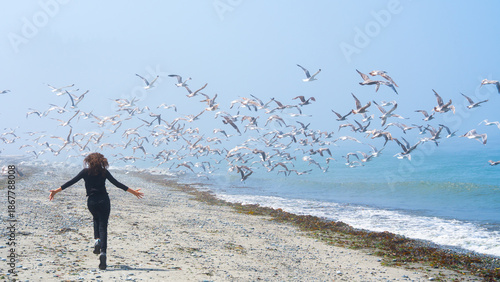 Rear view of a young girl running toward a flock of seagulls on a foggy sandy beach in Washington State