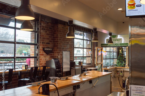 Obraz na plátne Spacious Modern Cafe Interior with Long Wooden Counters, Metal Chairs, Large Garage Style Windows, and Industrial Pendant Lighting, Creating a Bright and Welcoming Dining Space