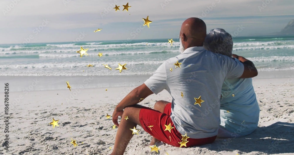 Fototapeta premium Sitting mature couple hugging facing ocean on white beach in summer clothes, gold stars, copy space