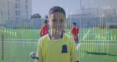Smiling child in yellow soccer jersey standing on urban field, showing soccer ball, goal overlay