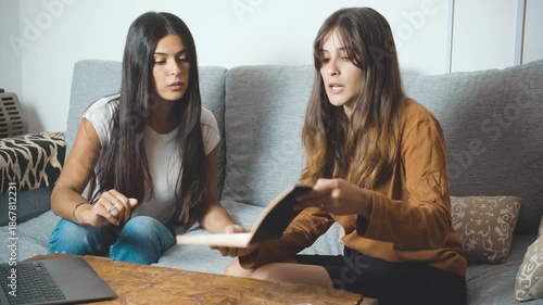 Two young women sitting on a couch at home, looking at a laptop and having a serious conversation. Female friends or colleagues discussing ideas during an online meeting, consultation, or remote work 