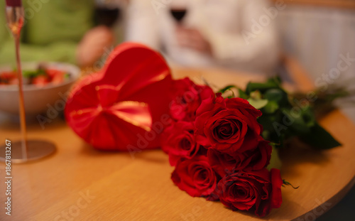 Close up of red roses bouquet and heart shaped gift box on wooden table during romantic dinner