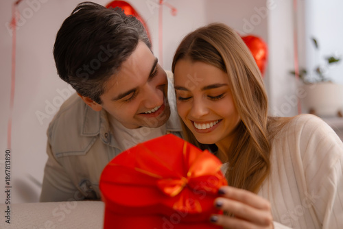 Smiling young man giving a red heart shaped present to his girlfriend for Valentine's Day celebration