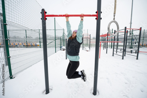 Girl hanging on a horizontal bar on a snowy sports ground in winter