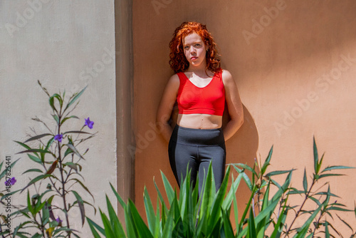 A woman in a red tank top and black pants stands in front of a wall