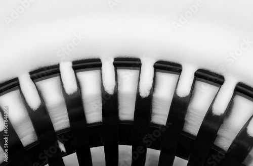 Closeup of part of a black exterior iron garbage can after a heavy snow, black and white, nobody