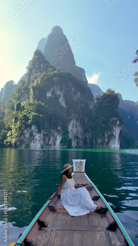 A traveler relaxes on a wooden boat, surrounded by the stunning emerald waters and dramatic limestone cliffs of Khao Sok National Park. Experience tranquility in Thailands nature.