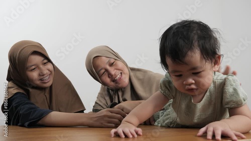 Happy Asian Muslim mother sitting on the floor and bonding with her two daughters