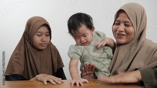 Happy Asian Muslim mother sitting on the floor and bonding with her two daughters