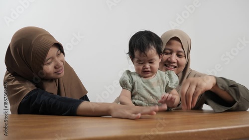 Happy Asian Muslim mother sitting on the floor and bonding with her two daughters