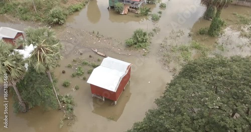Aerial view of a stilt house and a person in a small boat navigating floodwaters in a rural area.
