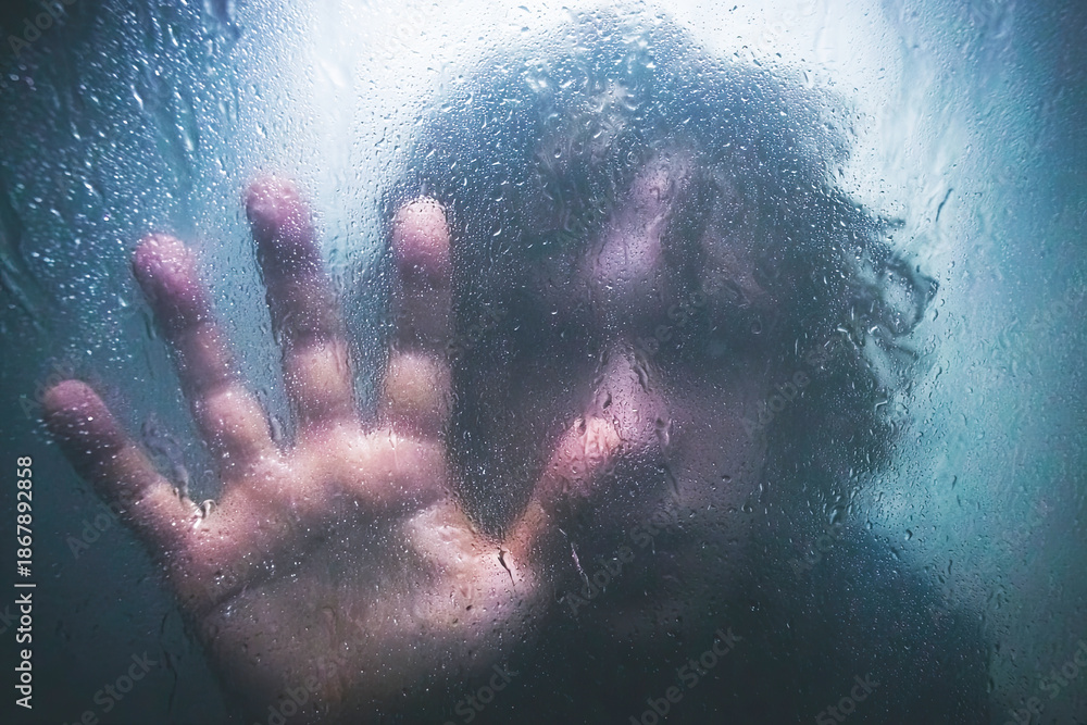 Obraz premium A person presses against a fogged glass surface, creating a sense of isolation and introspection, with water droplets adding to the mood.