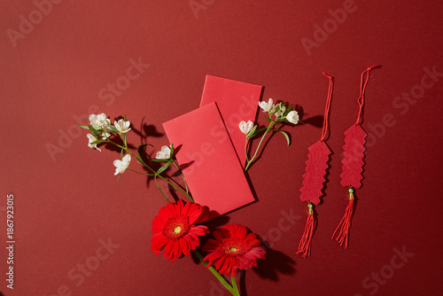 Chinese New Year flat lay featuring red envelopes, floral branches and festive elements decorated on red background. Clean layout for branding and advertising.