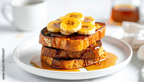 Stacked sourdough French toast with caramelized bananas and maple syrup drizzle on white plate