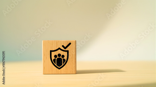 Symbolic wooden block showing a shield with people and a checkmark, representing validated group protection, team safety, and collective security assurance