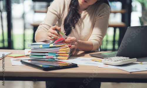 Photos Busy Workday: A person reviews documents at a desk, surrounded by office tools, papers, and tech, highlighting productivity and focus in a professional setting