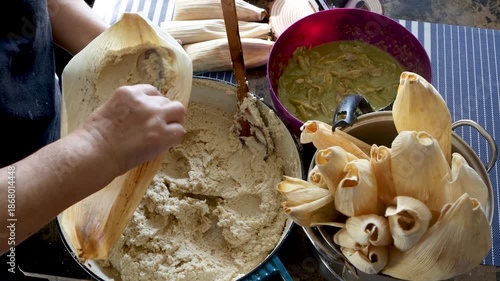 Unrecognizable woman spreading masa on a corn husk and adding chicken green chili filling