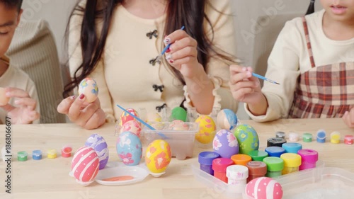 Easter egg painting. A mother and kids celebrate Easter indoors, using a paintbrush to decorate eggs near a festive basket.