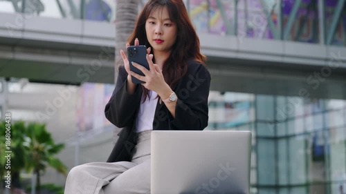 Confident business woman, elegant, on business walk, Thailand street building, makes phone call, works with laptop, modern urban setting.