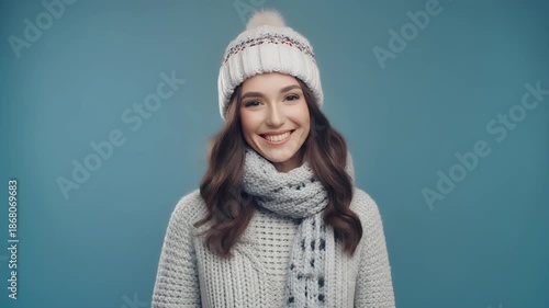Portrait Of A Young Woman Wearing A White Knit Sweater Scarf And Hat With A Blue Background