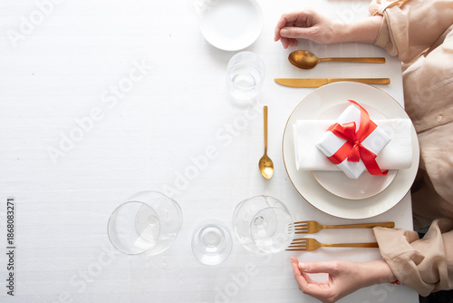 Minimalist banquet design featuring luxury dinnerware, golden fork, knife, spoon, glass, gift wrap, ribbon, napkin, white tablecloth, stylish dining, event, catering, holiday, birthday, Christmas.