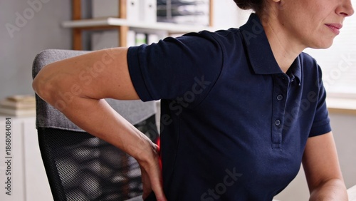 office syndrome in office worker concept, female touching her back suffering from muscle pain from sitting position during work. A woman experiencing back pain while sitting in an office chair.
