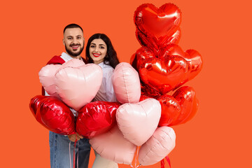 Young couple with heart-shaped balloons on orange background. Valentine's Day celebration