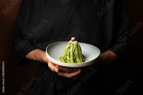Chef presenting a gourmet Matcha Mont Blanc dessert on a ceramic plate