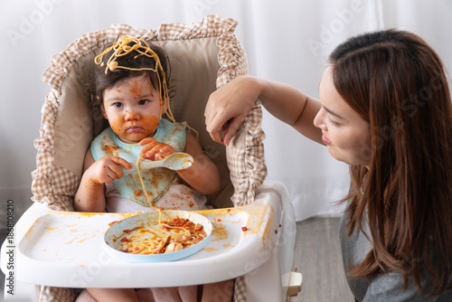 Cuadro en lienzo Funny messy baby girl holding spoon covered in spaghetti sauce on high chair