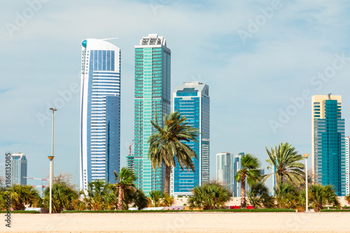 Sunny urban beachfront skyline with modern skyscrapers, palm trees, and clear blue sky