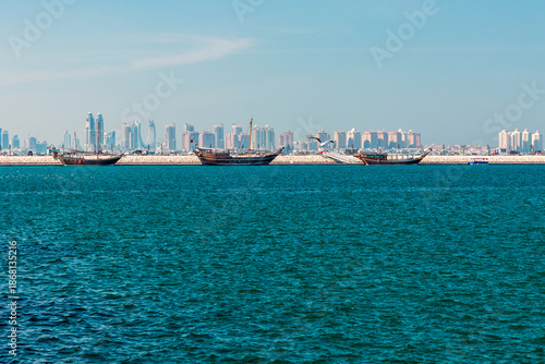 Doha, Qatar harbour boats with city skyline and calm blue sea under clear sky