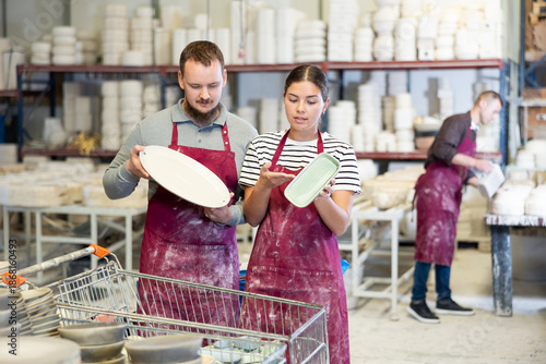 Slika na platnu Interested focused young girl and man in maroon work aprons, colleagues at ceram