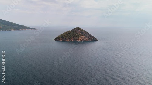 Scenic aerial drone approach toward Nisida Kinira Islet off the lush coast of Thasos, Greece, overlooking the turquoise Aegean Sea.
