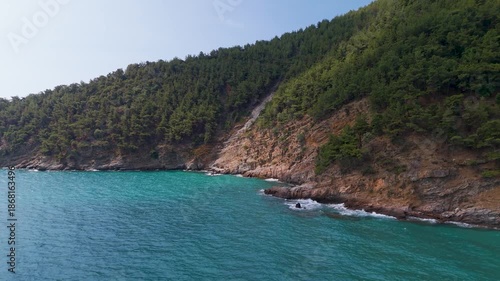 Aerial drone tracking shot panning low above the turquoise water along the pristine Kinira Beach and the densely forested coast of Thasos Island, Greece.