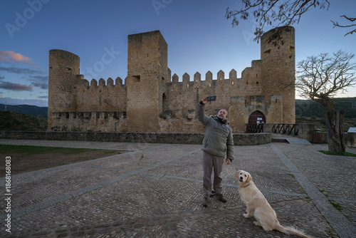 Man taking a selfie with his Golden Retriever dog at medieval Frias castle in Burgos Spain at sunset