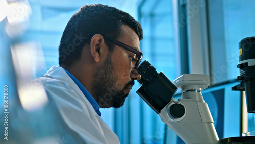 Fotografie A focused researcher in a lab coat examines a specimen under a microscope, highlighting precision and scientific inquiry in a modern lab