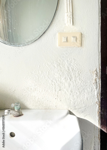 Broken Washbasin, Mirror and Light Switches on Damped, Musty Old Painted Wall with Sunlight. Textured Exterior Toilet Wall in Room at Dhamma Retreat Center, Saraburi, Thailand. 25 OCT 2025. A.M.