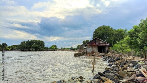 Rustic coastal hut beside mangrove lagoon under dramatic sky, showcasing peaceful rural life