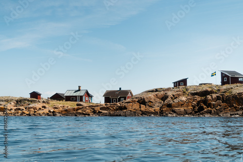 Traditional red wooden cottages on a rocky islet in Varberg archipelago, seen from the water, Sweden